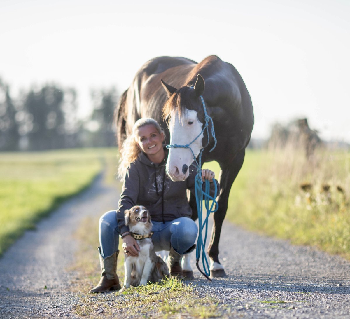 Caro kniet mit ihrem Pferd und dem Hund auf dem Feldweg