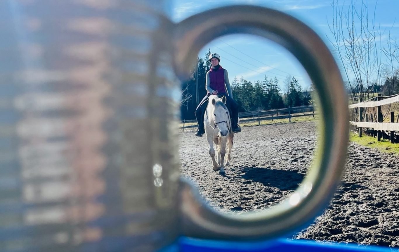 Blick durch einen Ring auf Caro mit einem Pferd auf dem Reitplatz